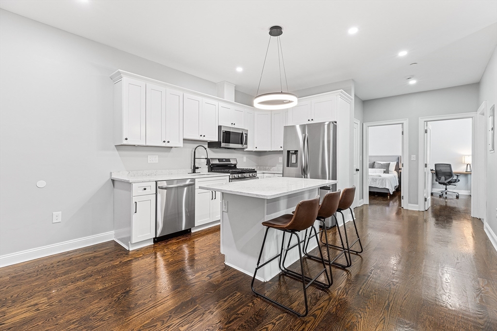 128 Hamilton Street, Unit 2B Boston, MA 02125 - Photo 7 of 23 a kitchen with stainless steel appliances a stove a sink a refrigerator and white cabinets with wooden floor