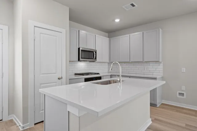 a kitchen with stainless steel appliances a sink a stove a microwave a sink a refrigerator white cabinets and wooden floor