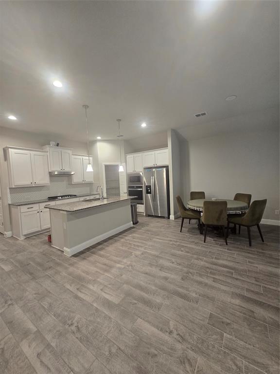 1704 Razorbill Road Denton, TX 76205 - Photo 17 of 20 Open-concept kitchen featuring an island with a breakfast bar, white cabinetry, stainless steel appliances, and wood-finish flooring