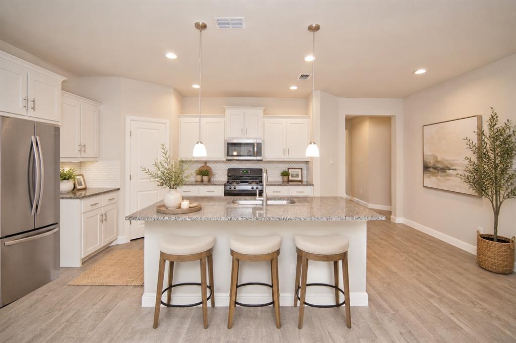 1804 Mensa Drive Haslet, TX 76052 - Photo 5 of 30 Kitchen featuring an oversized island with granite countertops, stainless steel appliances, white cabinetry, and wood-finish flooring
