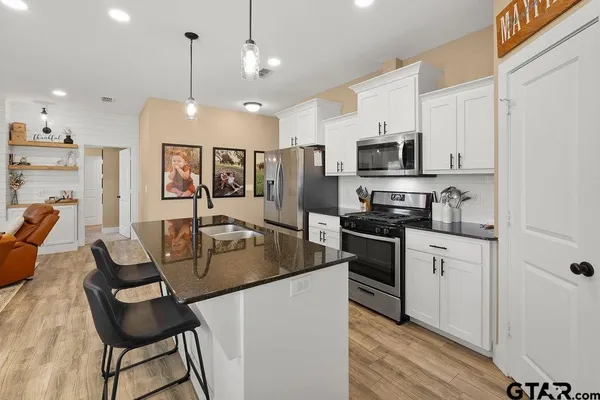 a kitchen with stainless steel appliances kitchen island granite countertop a stove a sink a microwave a refrigerator and white cabinets with wooden floor