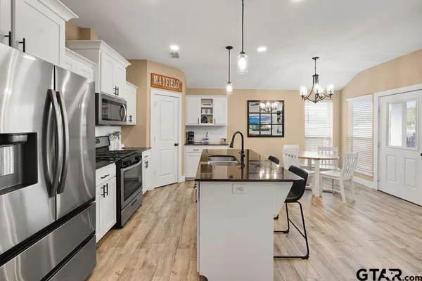 a kitchen with stainless steel appliances granite countertop a refrigerator a stove top oven a sink dishwasher a dining table and chairs with wooden floor
