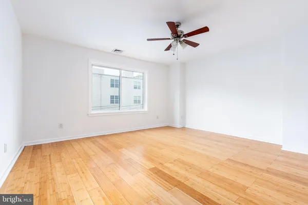a view of empty room with wooden floor and fan