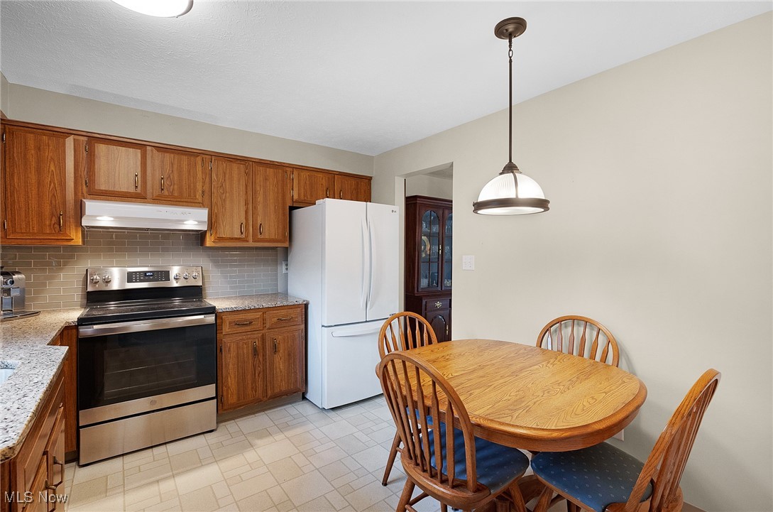 6474 State Road, Unit I10 Parma, OH 44134 - Photo 6 of 31 Kitchen with stainless steel electric range oven, tasteful backsplash, brown cabinets, freestanding refrigerator, and under cabinet range hood