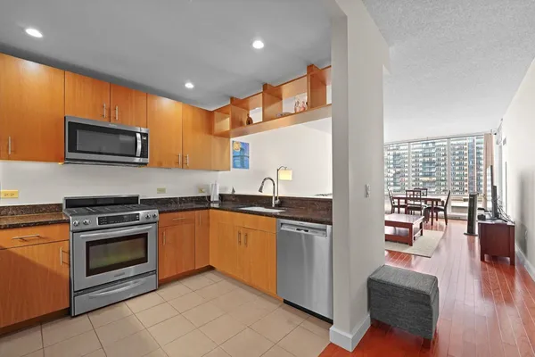 a kitchen with stainless steel appliances granite countertop a stove top oven a sink dishwasher a dining table and chairs with wooden floor