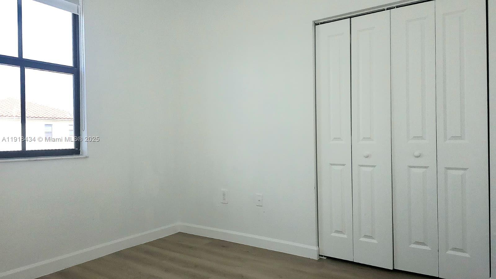11774 Southwest 246th Street, Unit 11774 Homestead, FL 33032 - Photo 12 of 18 a view of an empty room with wooden floor and a window