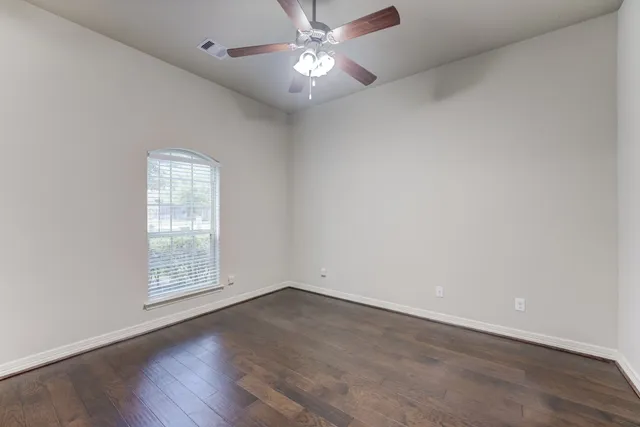 an empty room with wooden floor chandelier fan and windows