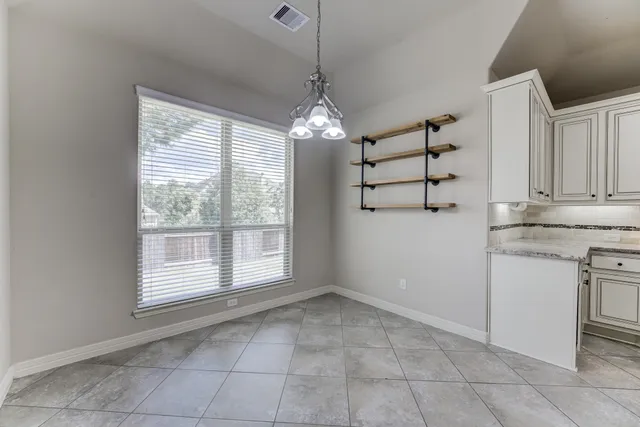 a view of an empty room with kitchen and window