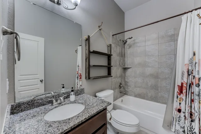 a bathroom with a granite countertop bathtub shower sink vanity mirror and toilet