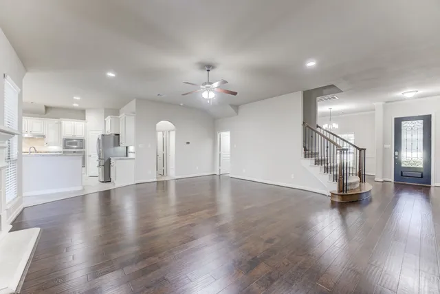 a view of an empty room with wooden floor and a kitchen