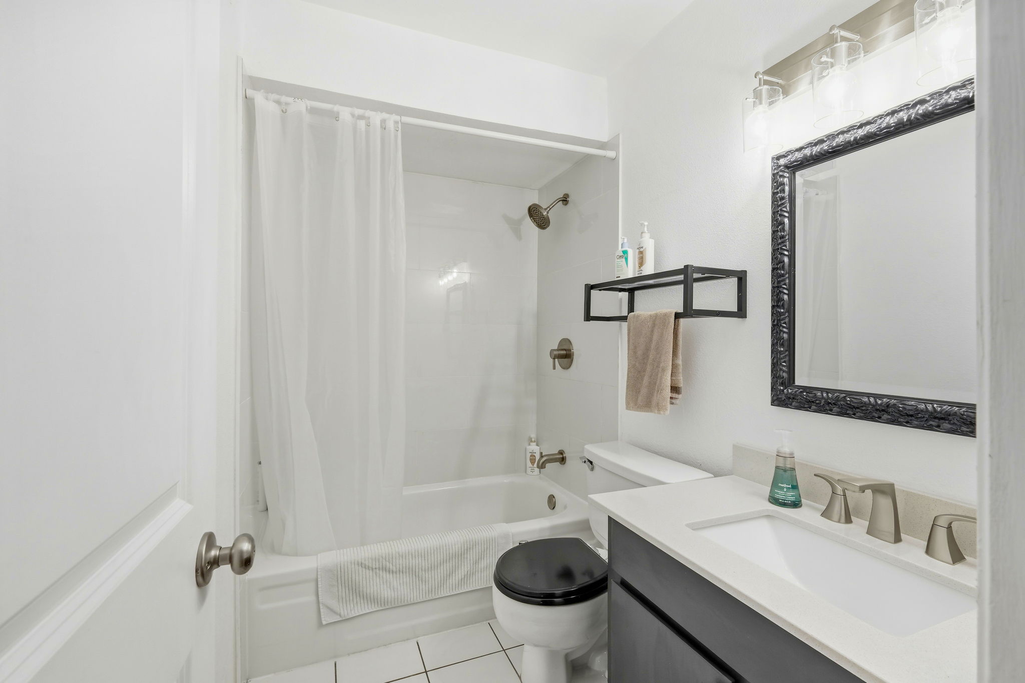 6910 Hart Lane, Unit 912 Austin, TX 78731 - Photo 14 of 36 Bathroom featuring a white subway tile tub surround, brushed nickel shower fixtures, a dark vanity with a white countertop, a black framed mirror, and white square floor tiles
