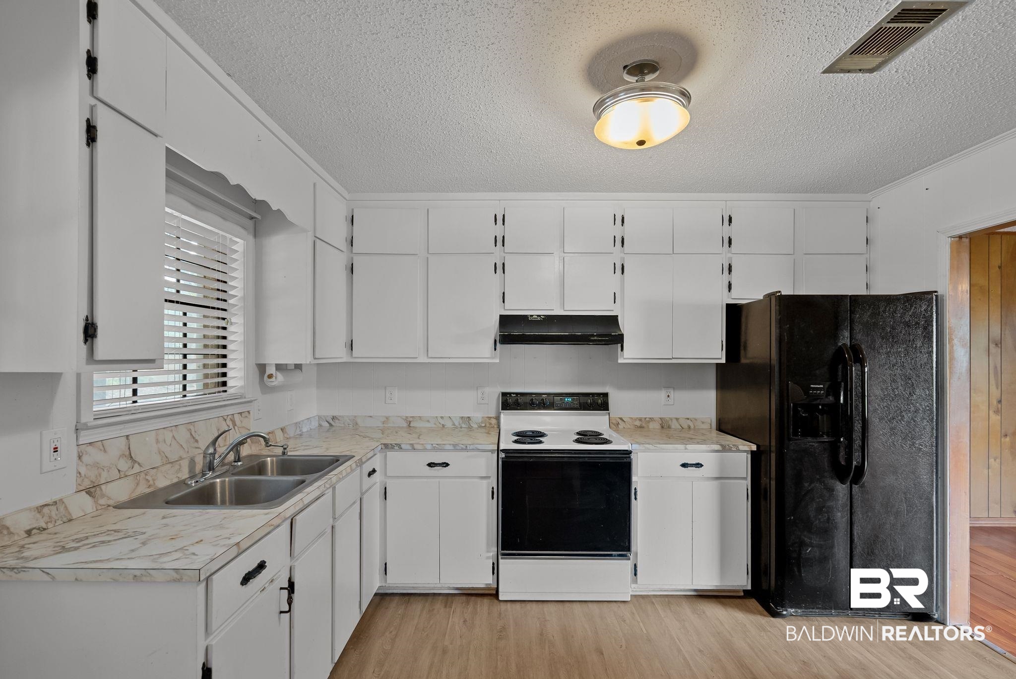 716 North Cedar Street Foley, AL 36535 - Photo 10 of 25 Kitchen featuring white cabinetry, patterned countertops with a backsplash, a double basin stainless steel sink, and wood-finish flooring