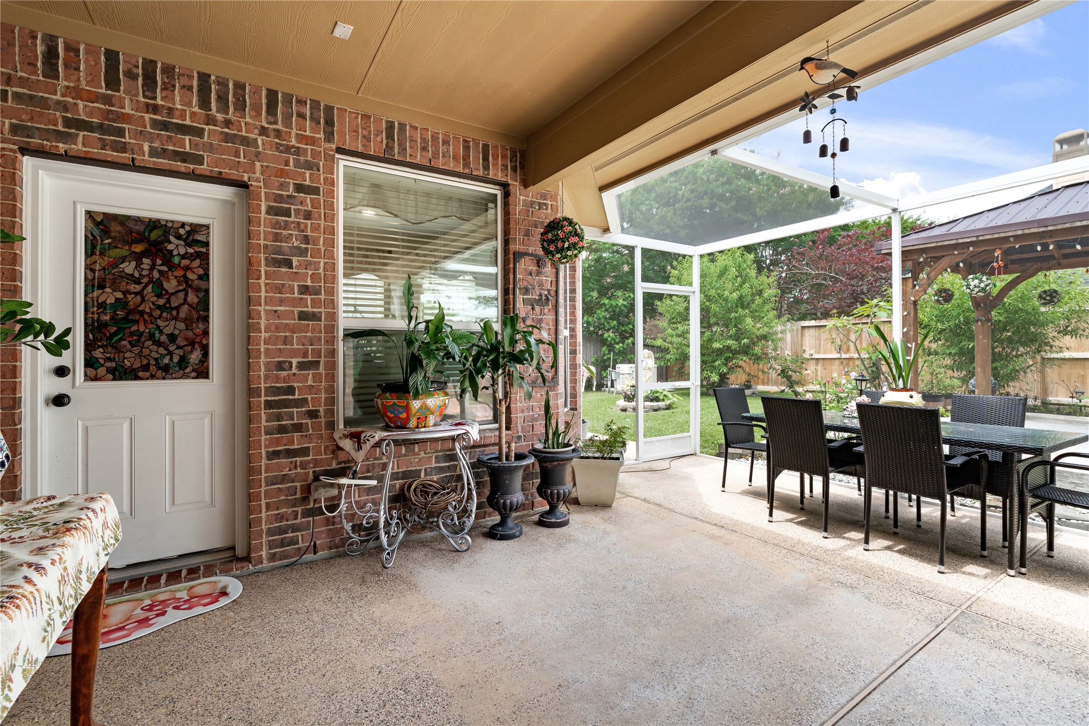 5802 Layton Meadows Lane Spring, TX 77379 - Photo 35 of 42 Covered back porch entry. Shows the stained glass back door, wind chimes, plants, decorative console table, and the screened dining area beyond. Great lifestyle shot.