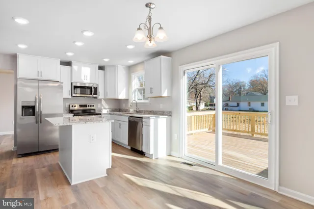 a kitchen with stainless steel appliances granite countertop a refrigerator a sink a stove and white cabinets with wooden floor