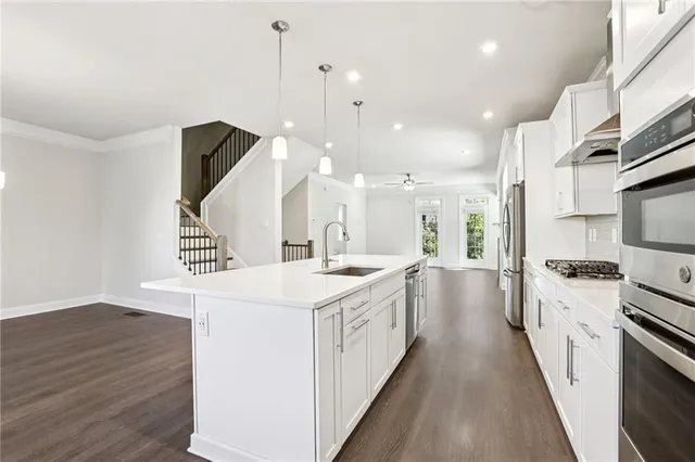 a large kitchen with stainless steel appliances a white stove top oven a sink dishwasher and a refrigerator with wooden floor