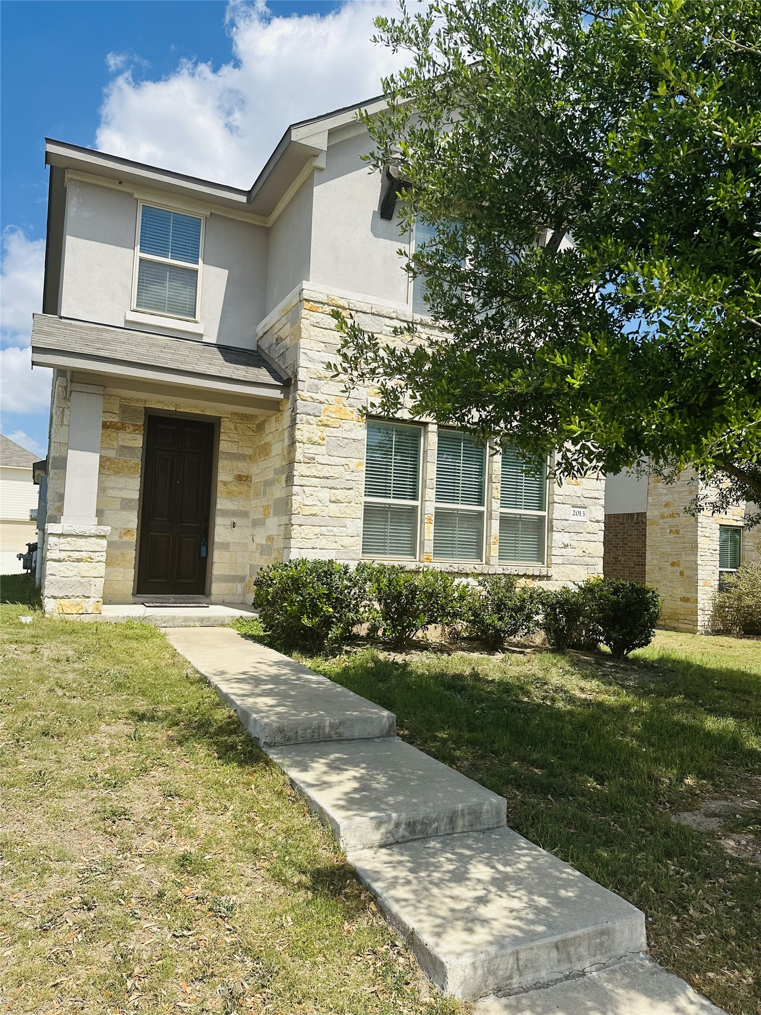 View of front of property featuring a front yard, stucco siding, and stone siding