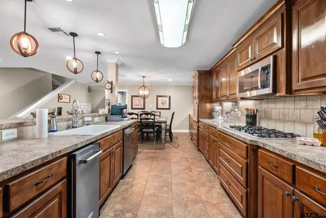 a large kitchen with stainless steel appliances granite countertop a stove top oven a sink dishwasher a dining table and chairs with wooden floor
