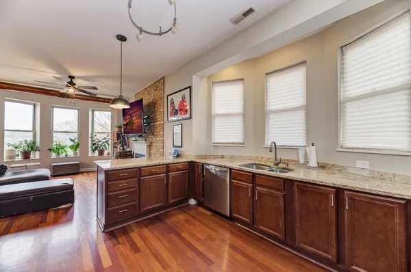 a large kitchen with granite countertop a sink dishwasher a stove and white cabinets with wooden floor