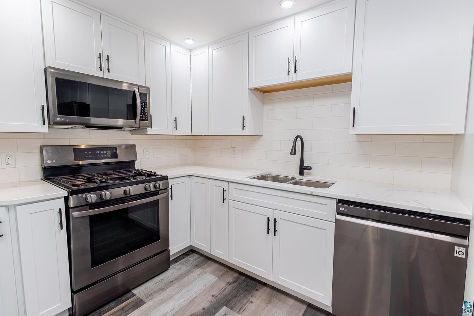 29 Ridge Road Esko, MN 55733 - Photo 12 of 41 Corner kitchen featuring white cabinetry with black hardware, white countertops, stainless steel appliances, and wood-finish flooring