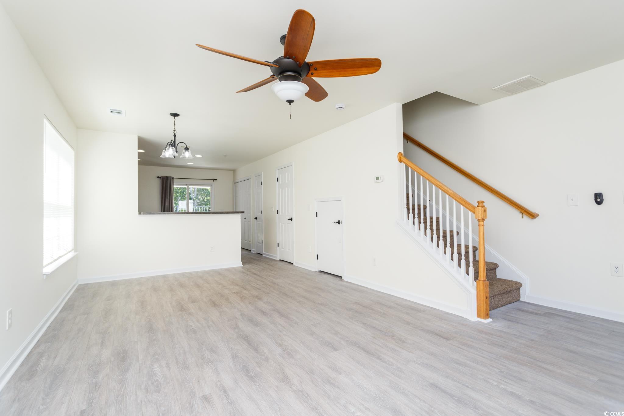 116 Barnacle Lane, Unit 1 Little River, SC 29566 - Photo 5 of 27 Unfurnished living room with stairs, light wood finished floors, a chandelier, and a ceiling fan