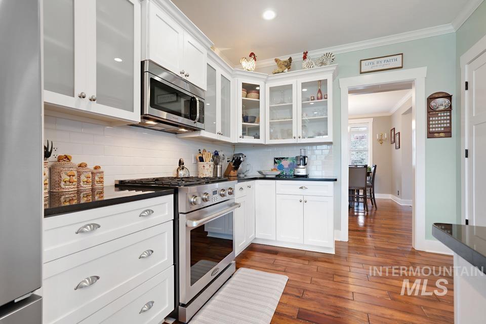 8271 Washoe Road Fruitland, ID 83619 - Photo 18 of 29 Kitchen featuring white cabinetry, stainless steel appliances, dark countertops, white subway tile backsplash, and wood-finish flooring