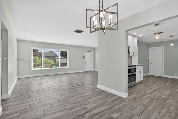 an empty room with wooden floor chandelier and windows