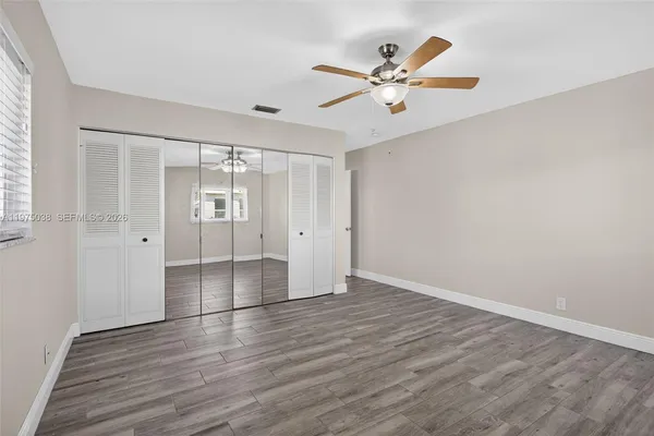 a view of an empty room with wooden floor and a ceiling fan
