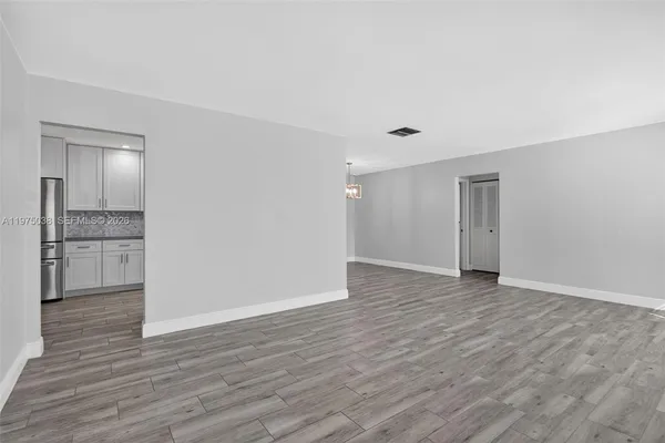 a view of an empty room with wooden floor and kitchen