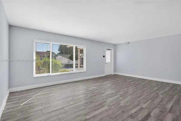 a view of an empty room with wooden floor and a window