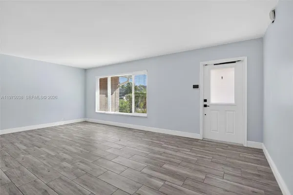 a view of an empty room with wooden floor and a window