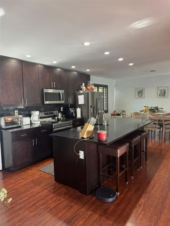 a kitchen with stainless steel appliances granite countertop a stove a sink dishwasher a microwave oven and a dining table with wooden floor