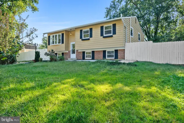 a house that is sitting in the grass with large trees and plants
