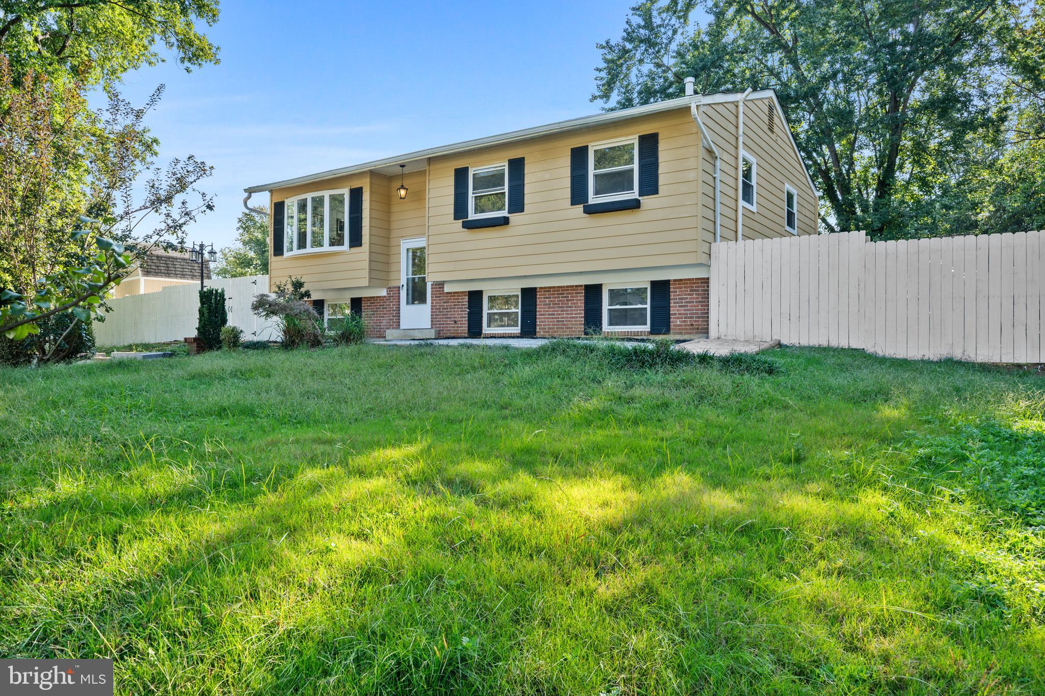 a house that is sitting in the grass with large trees and plants
