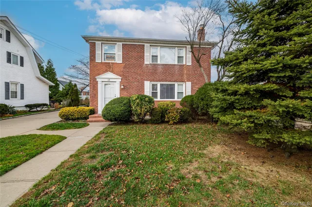 a brick house with a yard plants and large tree