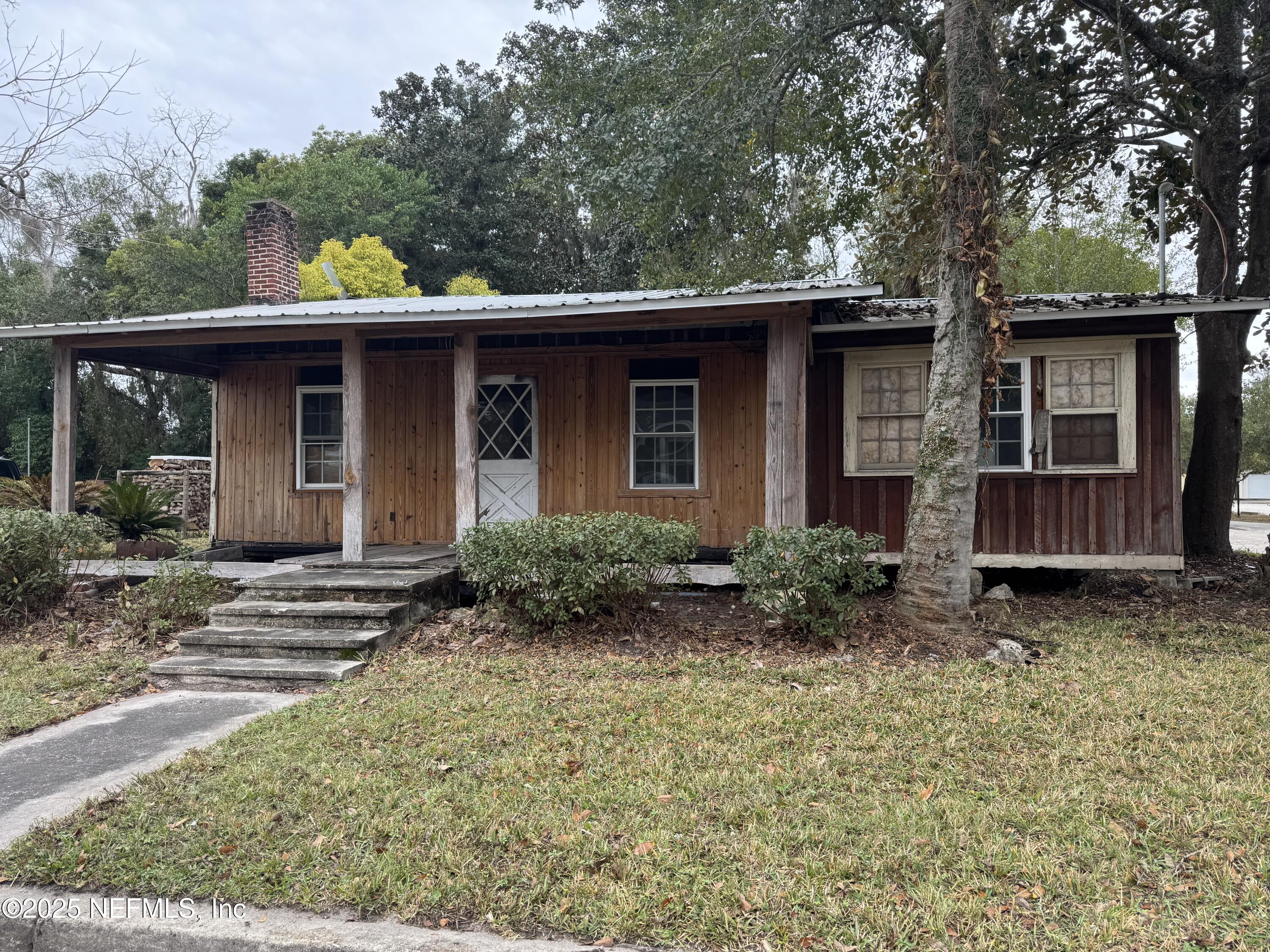 a view of a house with a yard plants and large tree