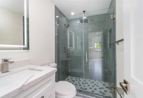 a bathroom with a granite countertop sink a toilet a mirror and shower