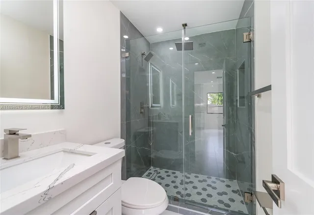 a bathroom with a granite countertop sink a toilet a mirror and shower