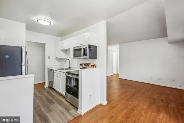 a kitchen with stainless steel appliances a stove top oven a sink a refrigerator white cabinets and wooden floor