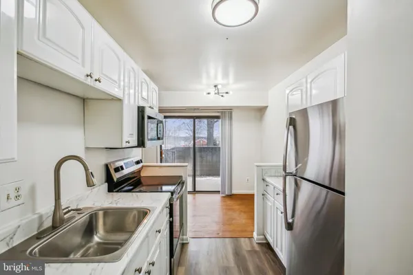 a kitchen with stainless steel appliances granite countertop a refrigerator a sink a stove and white cabinets with wooden floor