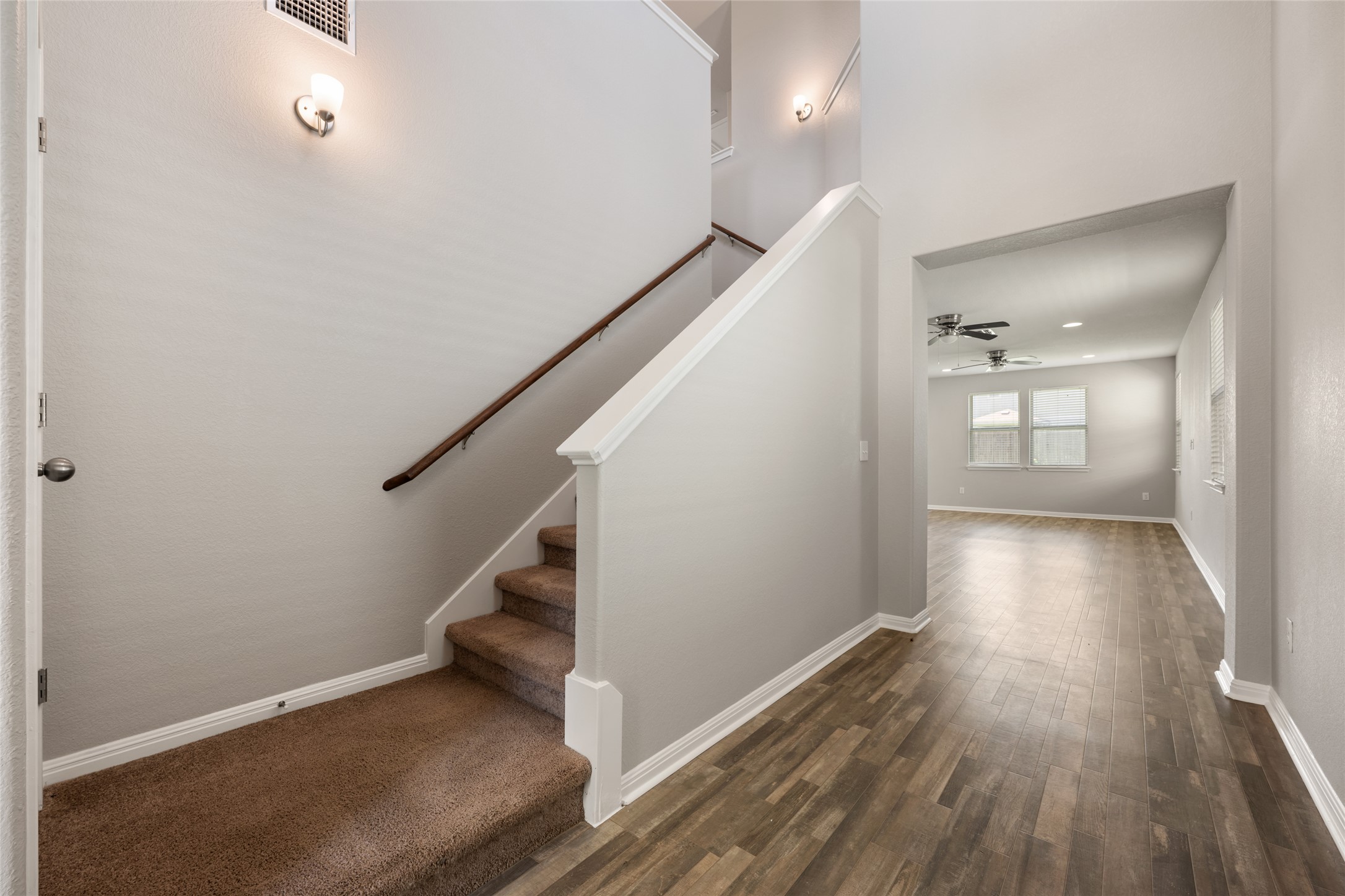 A welcoming entryway with rich wood-look flooring transitions to a carpeted staircase leading to upper levels.