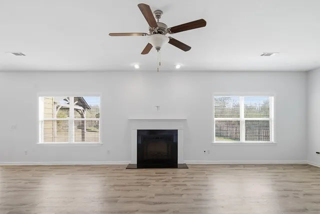 an empty room with wooden floor ceiling fan and windows