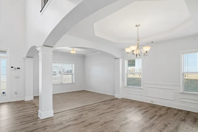 an empty room with wooden floor chandelier and windows