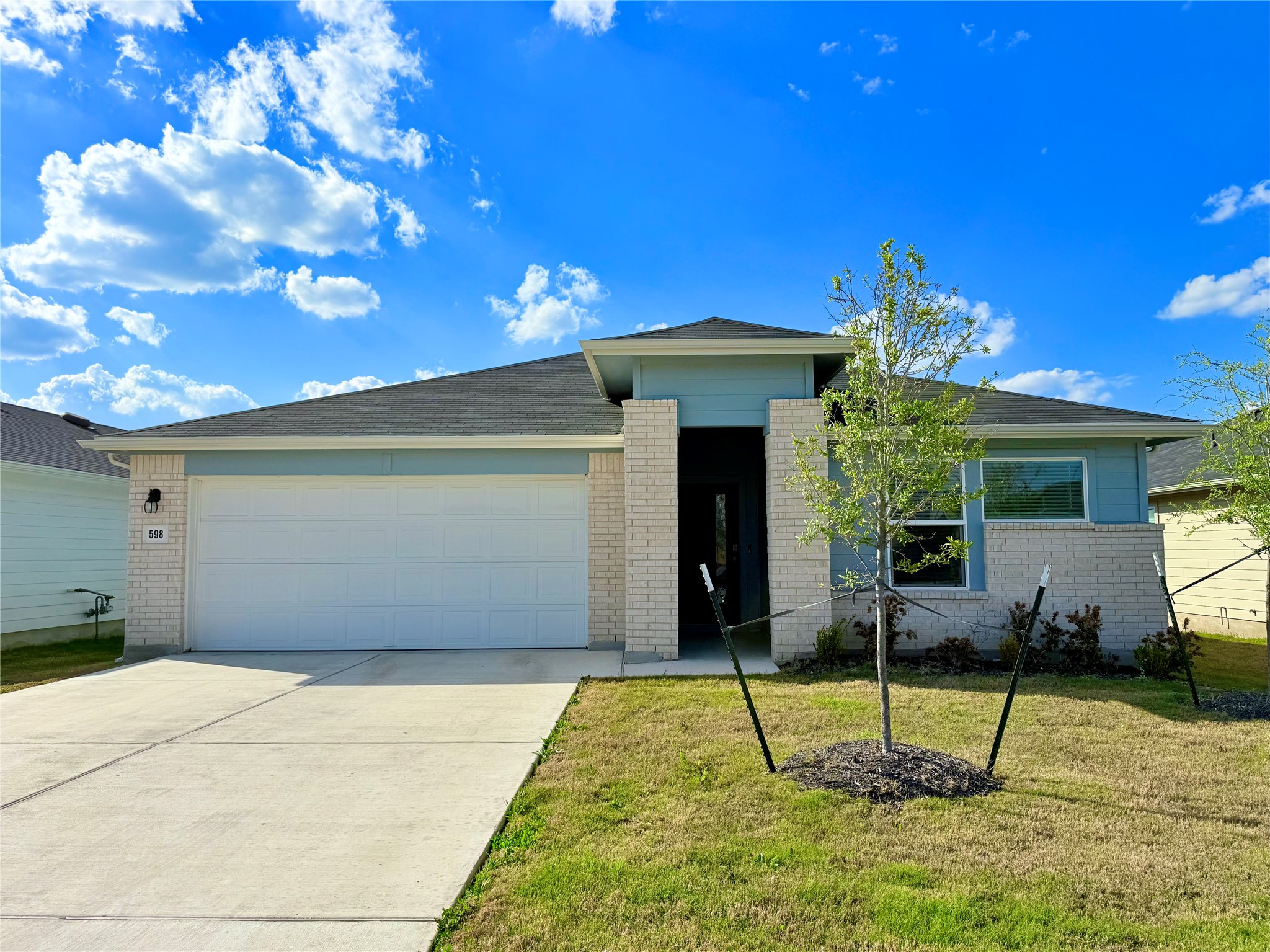 View of front of property featuring an attached garage, driveway, brick siding, and a front lawn