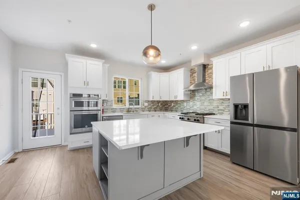 a large kitchen with kitchen island a stove a sink dishwasher a refrigerator and white cabinets with wooden floor