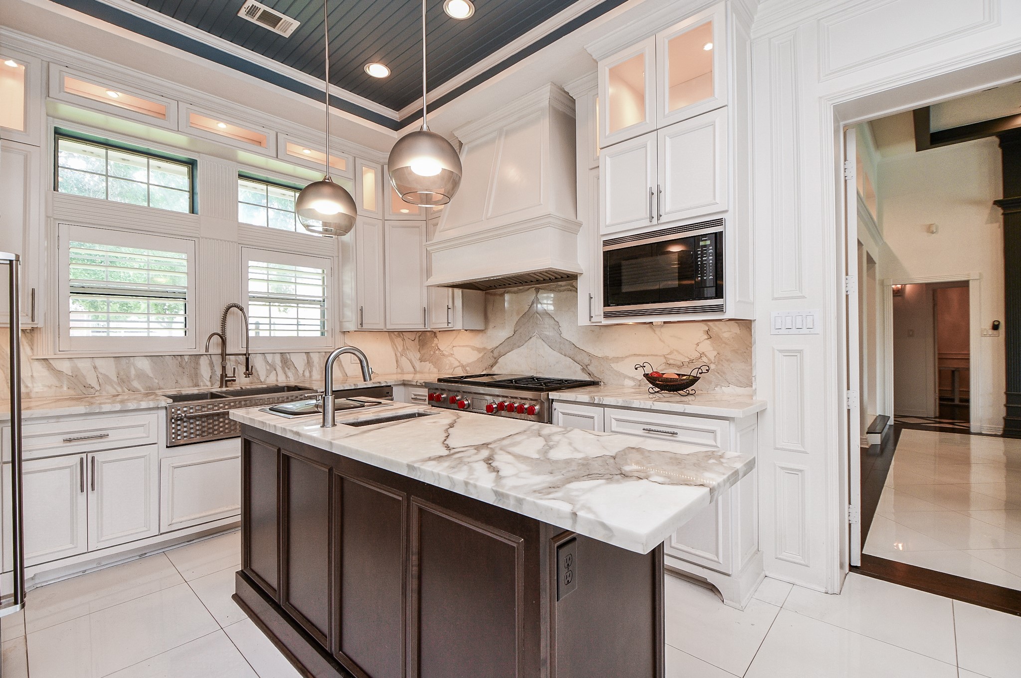 263 Wood Loop Street Houston, TX 77015 - Photo 25 of 45 This modern kitchen features elegant marble countertops, a central island with a sink, and high-end stainless steel appliances. It boasts custom white cabinetry, a stylish farmhouse sink, and large windows providing natural light. The space is accented with sleek pendant lighting and a sophisticated backsplash.