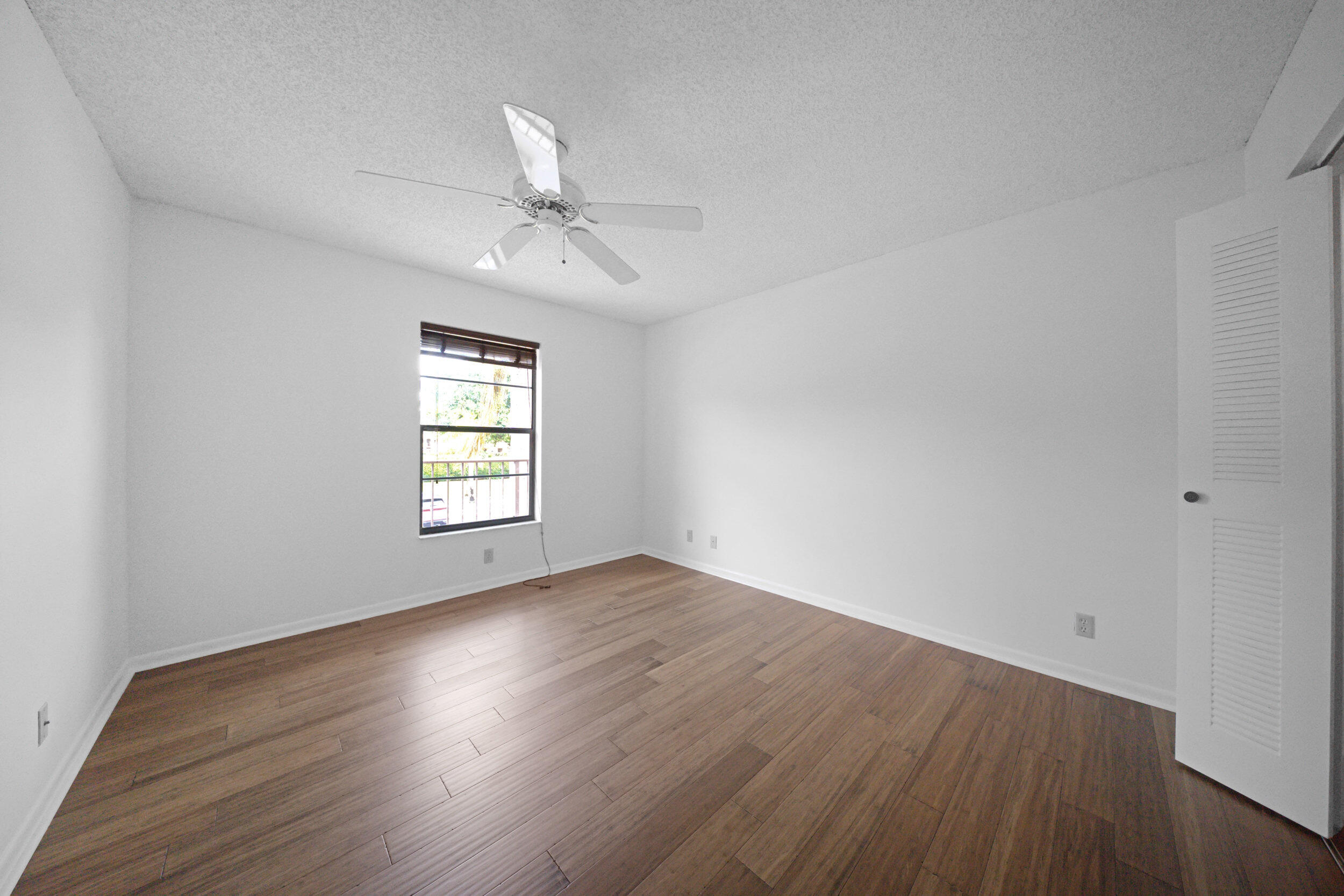 9480 Boca Cove Circle, Unit 415 Boca Raton, FL 33428 - Photo 18 of 25 an empty room with wooden floor ceiling fan and windows