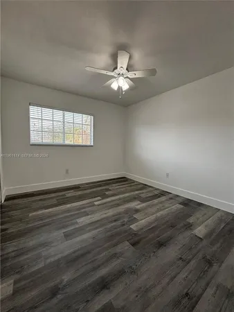 an empty room with wooden floor ceiling fan and windows