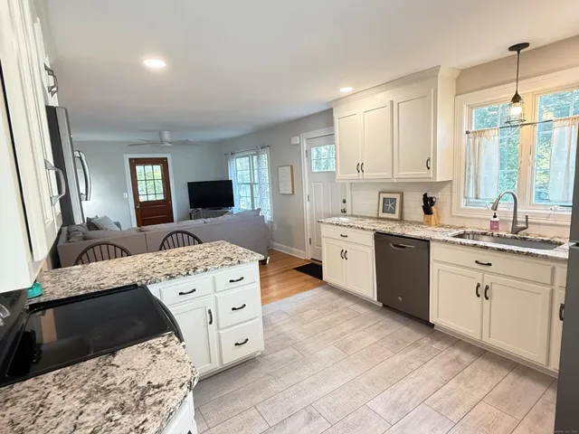 a large white kitchen with a stove a sink dishwasher and a refrigerator with wooden floor