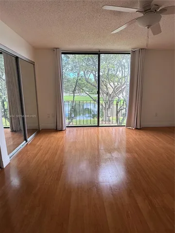 an empty room with wooden floor fan and windows