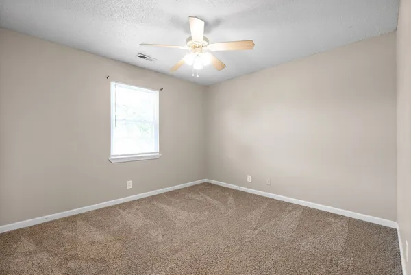 an empty room with a chandelier fan and windows